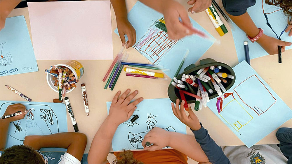 artigo-internacional-participacao-estudantes Várias crianças desenhando em uma mesa de escola