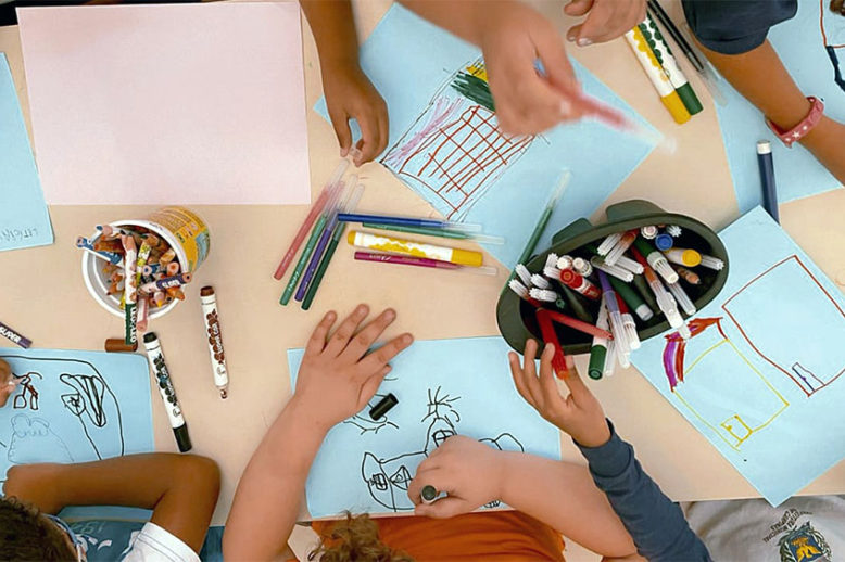 artigo-internacional-participacao-estudantes Várias crianças desenhando em uma mesa de escola