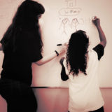 Psicóloga desenha no quadro branco junto com criança, na escola